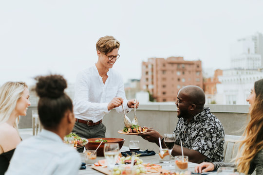 Man serving his friends salad at a rooftop party