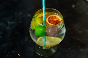 Refreshing, cold drink in a glass with colorful ice cubes and slices of citrus fruit