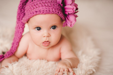 Cute baby girl wearing stylish knitted hat with flower decor closeup. Childhood.