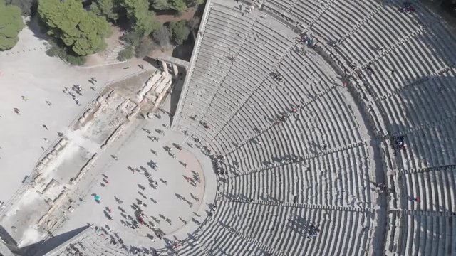 Twisting above the ancient theater of Epidavros in Greece, showing the people, the platforms and the theater scene. Clear sky, sunny weather, flat colour profile.
