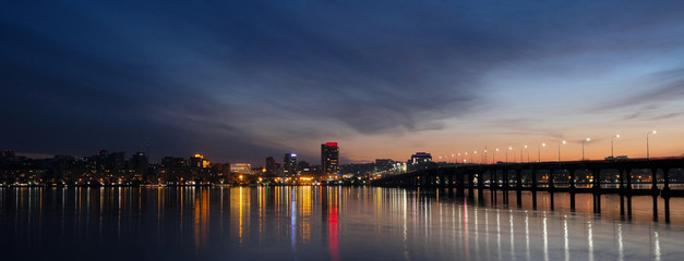 Panoramic view of the city at night. Night cityscape of the Dnieper near the river with reflection in the water with a bridge..