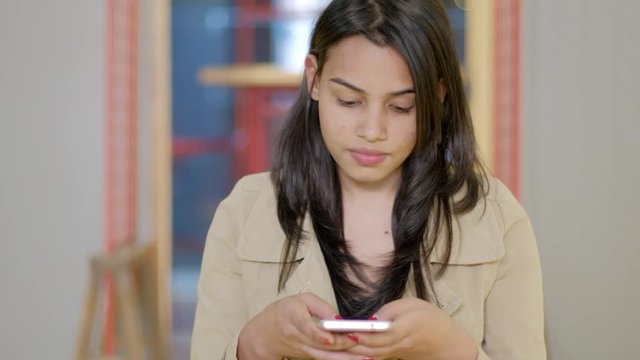 An attractive Indian young woman smiling and laughing, joy happiness, as she is busy texting messaging using her smart phone mobile communication device over wifi internet and looks at the camera 