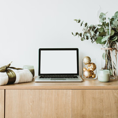 Blogger, freelance home office desk workspace. Laptop with mock up screen on wooden desktop decorated with eucalyptus bouquet, gift box, candles on white background.