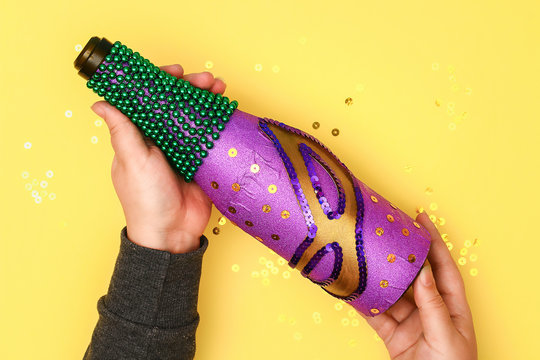 Diy Mardi Gras bottle purple adhesive paper, green bead, carnival mask, sequins yellow background.
