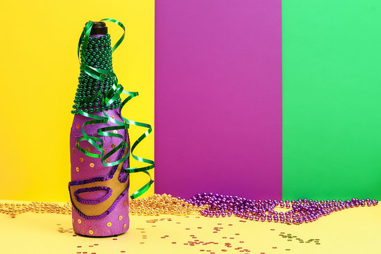 Diy Mardi Gras bottle purple adhesive paper, green bead, carnival mask, sequins yellow background.