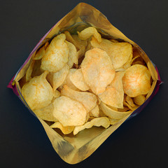 Crispy potato chips in a package on a black background, top view