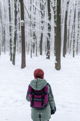 traveler girl with a bordo, red backpack walking on snow covered road in winter forest in frosty weather. vertical photo