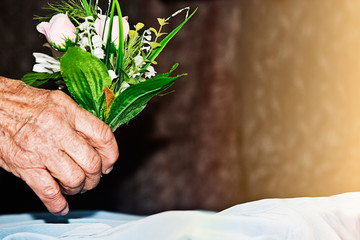 Old hand of grandmother with a bouquet of flowers in her hand