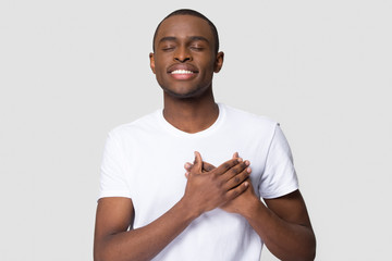 Grateful happy african man holding hands on chest feeling appreciation