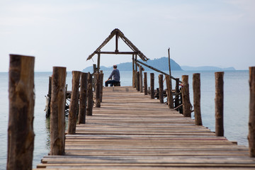 Fototapeta premium The old man sits on the pier and looks at the sea, the view from the back