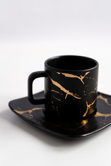 Black mugs with a saucer. Cups for coffee and tea on a white background. Utensils for any holiday, luxury wedding, birthday or party. Style Japanese art of repair broken dishes, kintsugi. Gold streaks