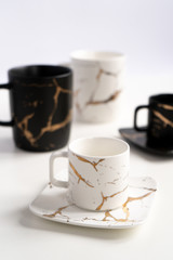 White and black mugs with a saucer. Cups for coffee and tea on a white background. Utensils for any holiday, luxury wedding, birthday or party. Style Japanese art of repair broken dishes, kintsugi.