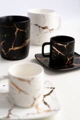 White and black mugs with a saucer. Cups for coffee and tea on a white background. Utensils for any holiday, luxury wedding, birthday or party. Style Japanese art of repair broken dishes, kintsugi.