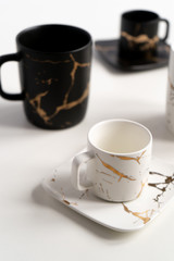 White and black mugs with a saucer. Cups for coffee and tea on a white background. Utensils for any holiday, luxury wedding, birthday or party. Style Japanese art of repair broken dishes, kintsugi.