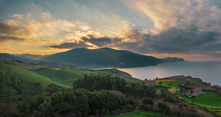 Aerial rural view of green fields and little villages on the hills; northen part of Spain; winter cloudy weather, evergreen plants and trees; fresh sea air, sun shining throug the dramatic sky, Bakio