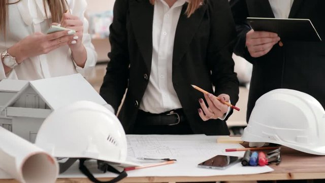 a group of engineers work in an office with a house plan. hold a digital tablet and discuss plans with each other. no faces.