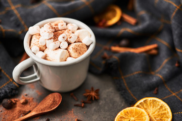 Hot cocoa drink with marshmallows in retro mug surrounded by ingredients: cinnamon, orange, anis and cove on black concrete table. Winter drink. Top view. Copy space for text.