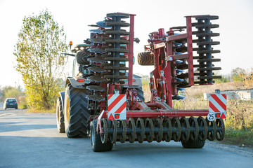 Tractor combine with disc harrows driving along rural road on sunny day. Agricultural machinery and...