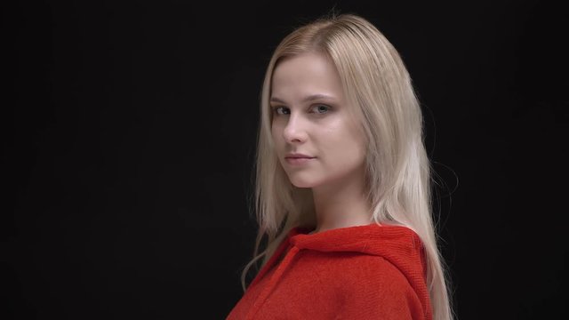 Portrait of young white-haired caucasian girl in red sweater turns to camera and watches calmly into camera on black background.