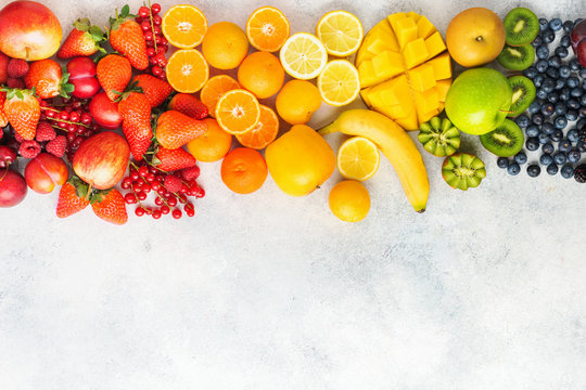 Rainbow fruits berries background on white. Top view of strawberries blueberries cherries mango apple lemons oranges red currants plums blackberries, selective focus