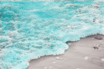 Close up blue sea water waves with white bubbles on sand beach