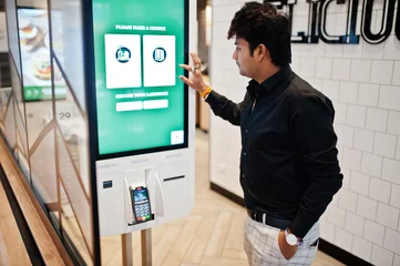 Deurstickers Indian man customer at store place orders and pay through self pay floor kiosk for fast food, payment terminal. Make a choise of language on screen. © AS Photo Family