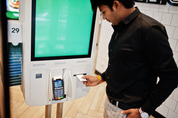 Indian man customer at store place orders and pay through self pay floor kiosk for fast food, payment terminal. His taking fiscal check.