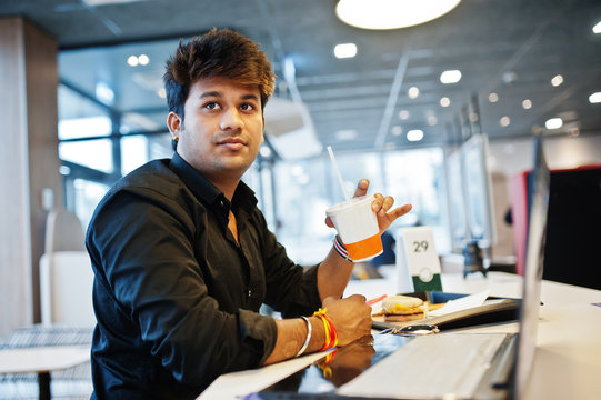 Stylish Indian Man Sitting At Fast Food Cafe Against His Laptop And Drink Soda.