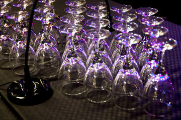 Blurred photo of wineglasses or goblets on table. A game of reflected purple and pink light on a black background. Effect of bokeh