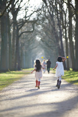 Two cute Asian sisters dressed in white having fun outdoors in a park playing with flowers and running around