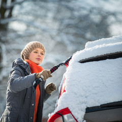 Pretty, young woman cleaning her car from snow after heavy snowstorm (color toned image)