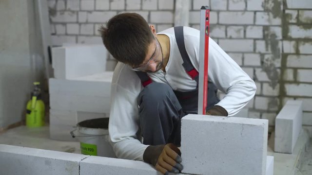 construction worker checking evenness of aerated concrete wall with bubble level