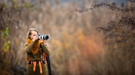 Pretty, female photographer taking pictures outdoor on a lovely autumn day - shallow DOF, color toned image