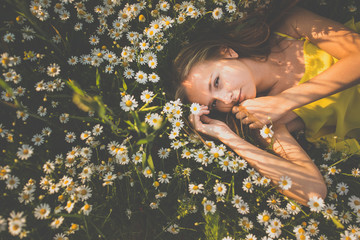 Portrait of young  woman with radiant clean skin lying down amid flowers on a lovely meadow on a...