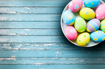 easter, holidays and object concept - close up of colored eggs on plate over blue vintage wooden boards background