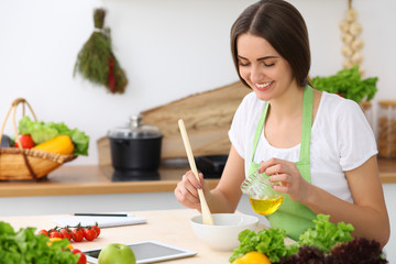 Beautiful Hispanic  woman cooking while using tablet computer in kitchen or  making online shopping by touchpad and credit card. Housewife found new recipe for dinner