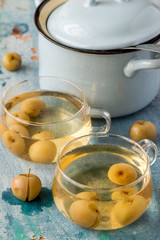 Homemade compote of small apples in glass transparent mugs, next to a saucepan on an old wooden table. Selective focus.