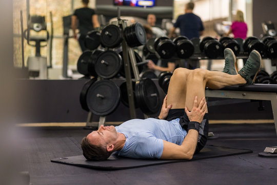 Image of a muscular man using a bench to make abdominal exercise at the gym.