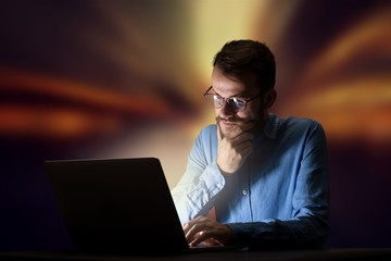 Young handsome businessman working late at night in the office with warm lights in the background