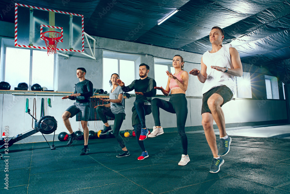 Wall mural Shot of young men and women at the gym. Functional fitness workout. The group of people during training session. Fit athletic models. Healthy lifestyle concept