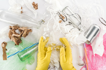 Cropped view of man holding empty plastic bottle among can, glass bottles, plastic bags, paper strips, paper and plastic tubes
