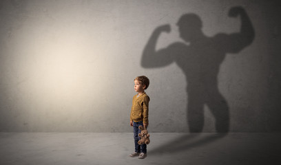 Little waggish boy in an empty room with musclemen shadow behind
