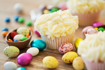 Fototapeta na wymiar easter, food and holidays concept - frosted cupcakes with chocolate eggs and candies on table