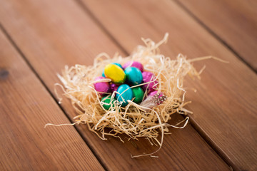 easter, confectionery and holidays concept - chocolate eggs in straw nest on wooden table