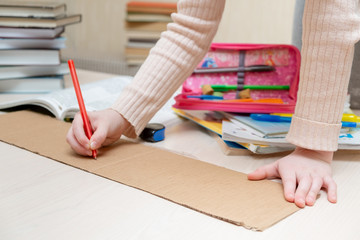 child draws on a piece of cardboard. close-up. there are books and pencils nearby