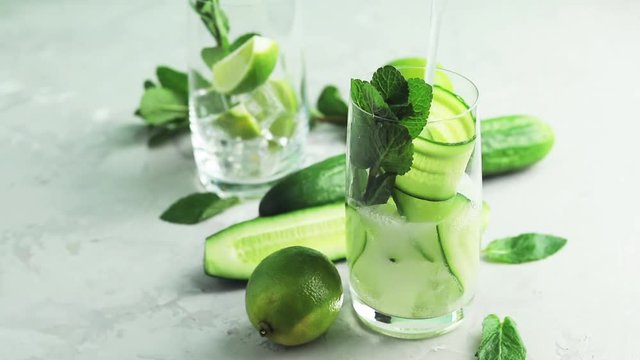 Pouring detox cocktail of mint, cucumber and lemon in highball glasses on a gray concrete stone surface background. With copy space for your text, close up, shallow depth of the field, 59.94 fps