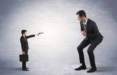 Fototapeta premium Tiny businessman with gun shooting giant fearful businessman 