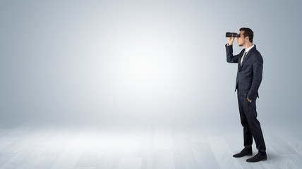 Businessman looking forward with binoculars in an empty space
