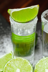 Tequila silver shots with lime slices and salt on wooden board