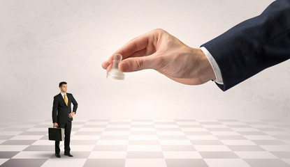 Fototapeta premium Small businessman fighting against big chessman on a big hand with chess board concept 